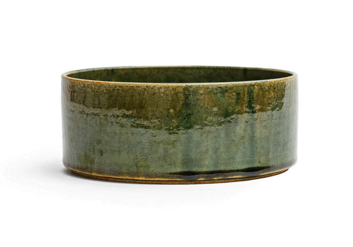 Silhouetted image of large ceramic oribe bowl with deep green glaze by Time and Style against white background.