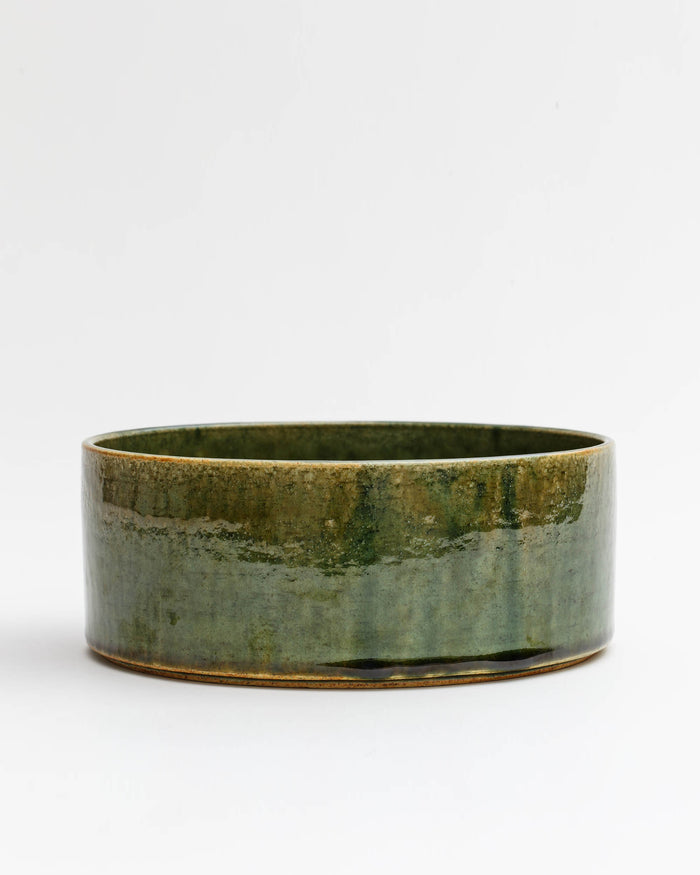 Silhouetted image of large ceramic oribe bowl with deep green glaze by Time and Style against white-gray background.