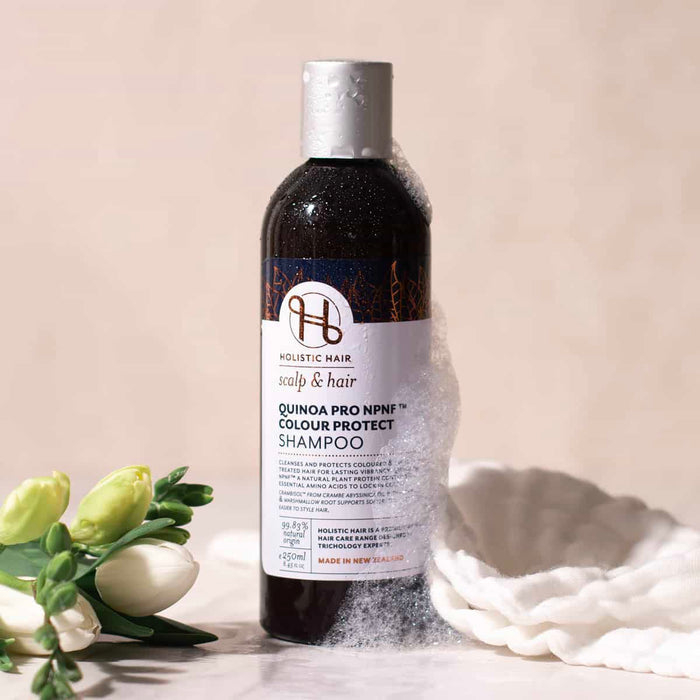 Bottle of Holistic Hair Colour Protect Shampoo with flowers and a white cloth on a beige background.