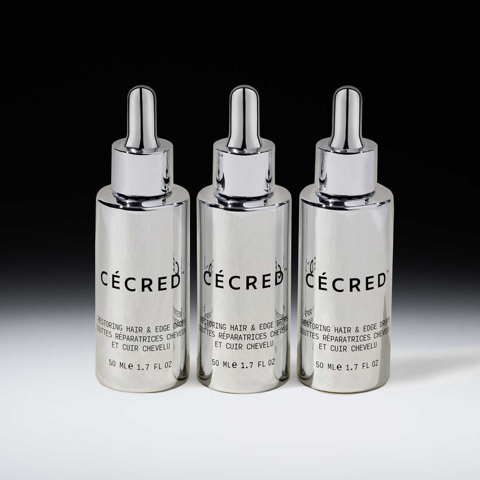 Three Cécred Restoring Hair & Edge Drops 50ml silver dropper bottles displayed together against a gradient grey background