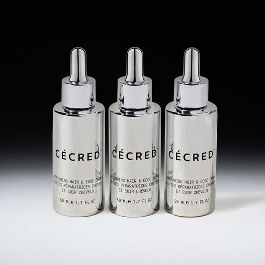 Three Cécred Restoring Hair & Edge Drops 50ml silver dropper bottles displayed together against a gradient grey background