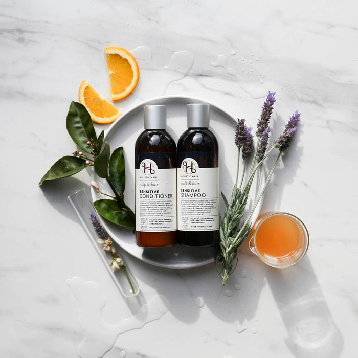 Two bottles of sensitive shampoo and conditioner on a white surface with lavender and orange slices.