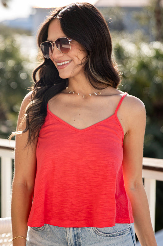 Woman wearing a red tank top and denim shorts on a balcony.
