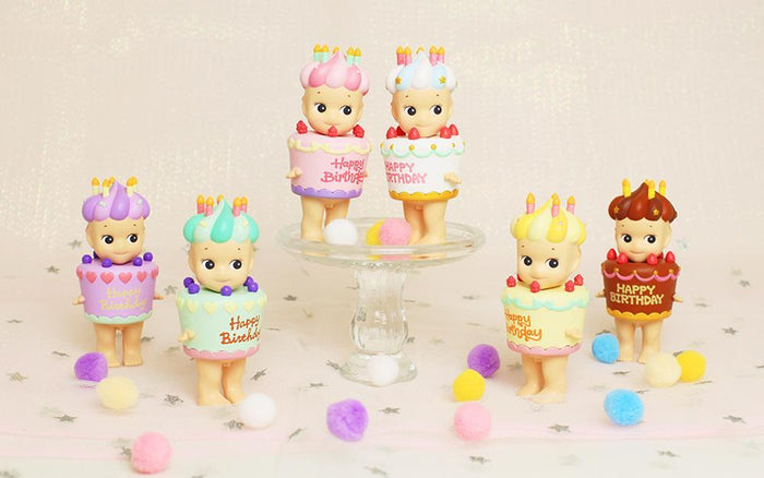 A group of toy figurines on a table, including Sonny Angel birthday cake characters from the Blind Box Series.