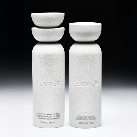 Two white cylindrical bottles with matching bowl-shaped caps labeled "Cécred," containing clarifying and hydrating shampoos.