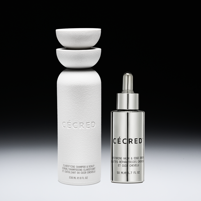 Two white and silver CÉCRED hair care bottles with bowls stacked on top of the larger bottle against a black background.