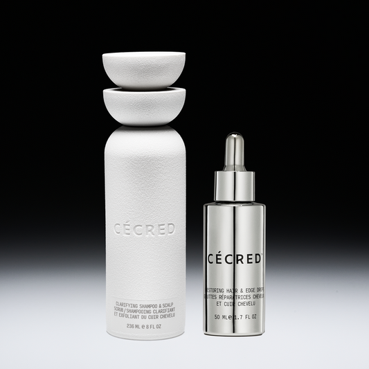 Two white and silver CÉCRED hair care bottles with bowls stacked on top of the larger bottle against a black background.