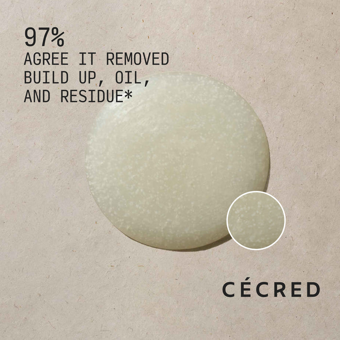 Close-up of Cécred Clarifying Shampoo & Scalp Scrub formula with exfoliating beads and 97% Agree It Removed Buildup, Oil, and Residue claim text against a warm neutral textured background