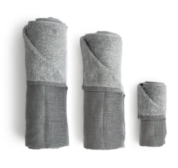 Silhouetted body, hand, and face zen charcoal towels rolled up placed next to each other, against white background.
