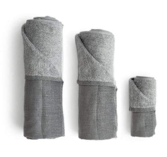Silhouetted body, hand, and face zen charcoal towels rolled up placed next to each other, against white background.