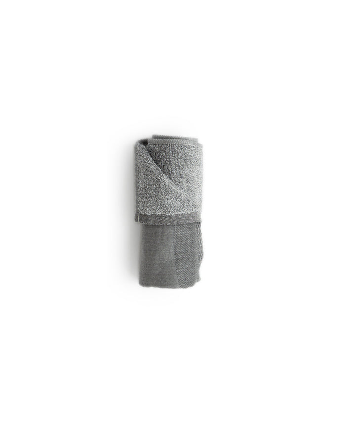 Face size zen charcoal towel rolled up silhouetted against white background.